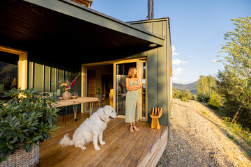 A woman and her dog enjoy a peaceful evening on the terrace of a modern countryside home. The warm...
