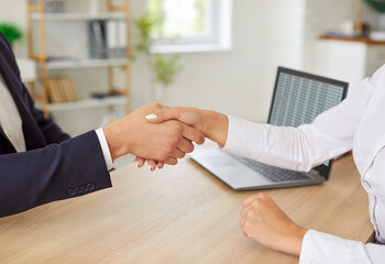 Close-up shot of business people shaking hands in an office setting. The handshake signifies...