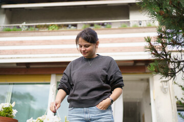 cute smiling brunette girl with pinned up hair in sweatshirt and jeans standing in front of her house. happy life concept