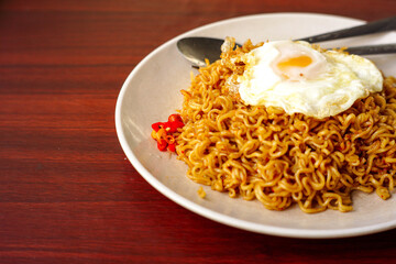 a fried instant noodle with egg toping and chili with wooden background