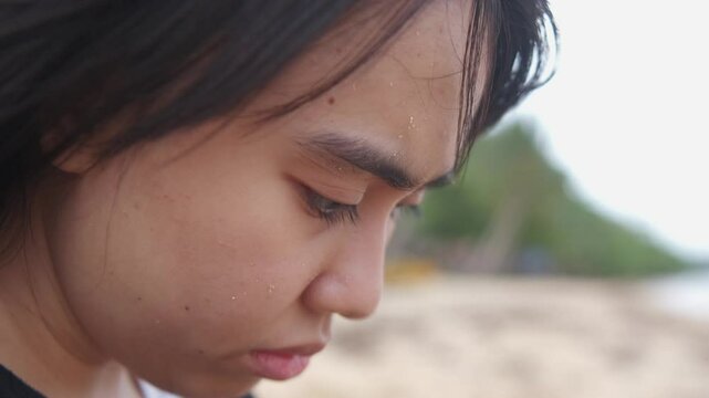 Static closeup shot of depressed young woman's face dramatically looking at horizon with wind blowing at beach setting.