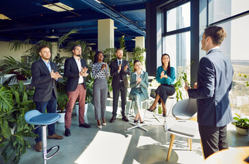 Male trainer or team leader making presentation at corporate meeting for diverse colleagues. Group of happy business people in formalwear applauding and thanking man speaker for business presentation.
