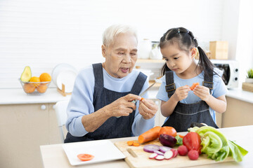 senior woman cutting fresh tomato and vegetables and giving to granddaughter in the kitchen