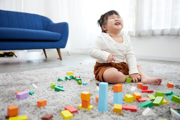 child girl feeling happy and playing with colorful toy blocks on the carpet floor