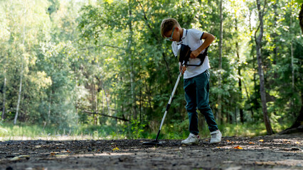 A boy with a metal detector in the park is looking for treasure
