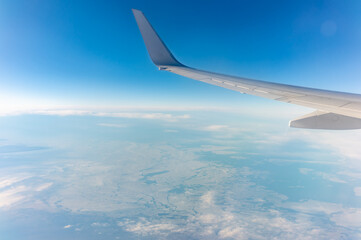 Obraz premium View from the airplane window at a beautiful blue clear sky, earth, sea and the airplane wing