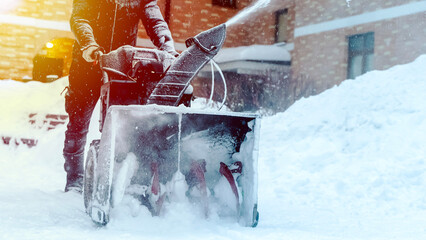 a man removes snow with a snow blower in the yard of a house