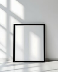 A black framed poster mockup on a white wall with shadows.