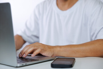 Middle-aged man in white shirt using laptop and smartphone on white background