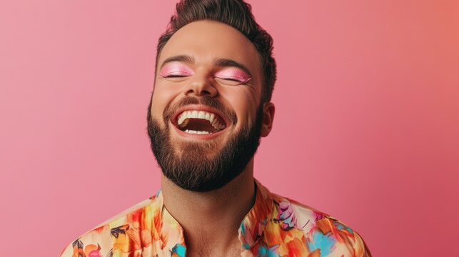 Man with a beard and pink eye shadow is smiling and laughing. He is wearing a colorful shirt with a floral pattern