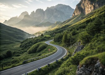 Naklejka premium Serpentine Mountain Road Winds Through Lush Green Valleys Shrouded in Mist and Nature's Beauty