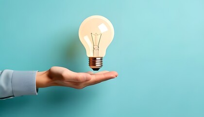 A hand holding a glowing light bulb against a pastel blue background, symbolizing ideas, innovation, and creativity.
