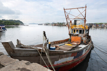 Obraz premium A colorful traditional wooden fishing boat, equipped with tools and gear, is docked at the local fishing pier, transporting fish from the boat to the market in Phuket, Thailand.