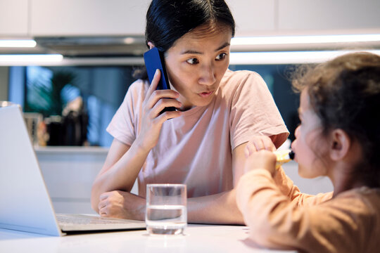 Mother shushing daughter and talking on smart phone at home