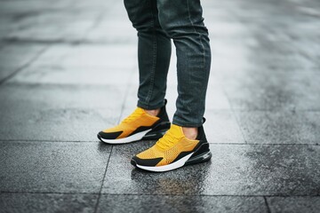 Man wearing yellow sneakers standing on wet pavement