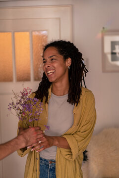 Friend giving flowers to woman standing at home