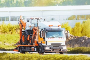 Tow truck with mini excavator on a highway on a sunny countryside summer day