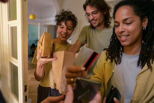 Woman doing online payment with friend holding package at doorway