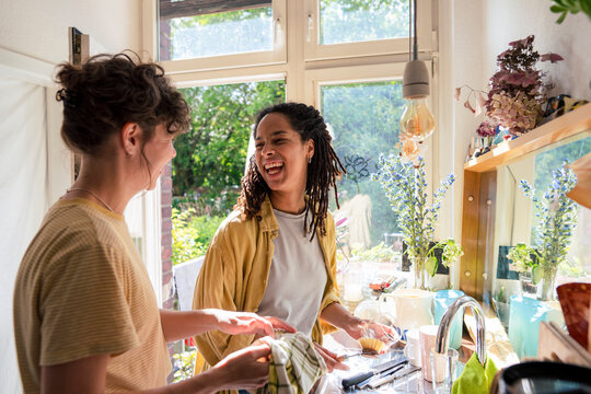 Happy multiracial friends doing chores in kitchen at home