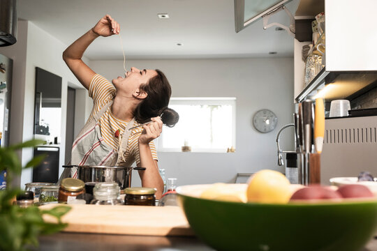 Happy young woman eating spaghetti and cooking food in kitchen at home