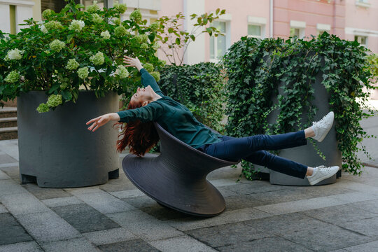 Happy businesswoman balancing on spun chair in urban garden