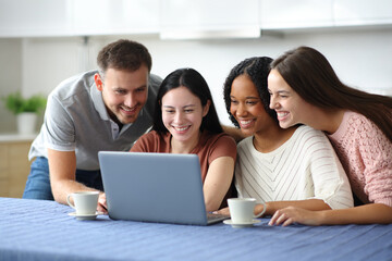 Four interracial happy friends checking laptop at home