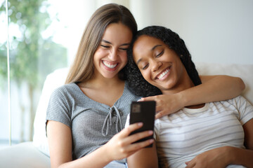 Happy interracial lesbian couple checking cell phone on a sofa