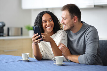 Happy couple checking phone looking each other in the kitchen