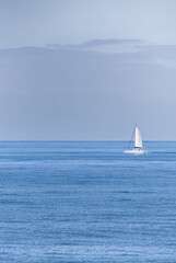 Obraz premium A minimalist image of a lone yacht sailing on a calm blue sea.