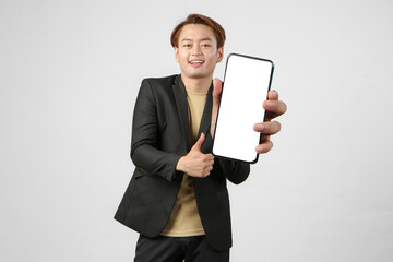 portrait of happy asian businessman wearing suit holding mobile phone and showing blank screen  giving thumb up gesture on isolated background.