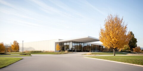 Obraz premium Modern building with glass facade surrounded by autumn trees and blue sky.