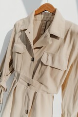 Elegant beige shirt dress hanging on a wooden hanger, showcasing its design against a bright background in natural light