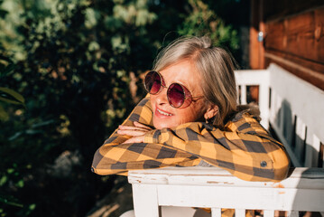 Beautiful older women is sitting in front of her cabin, enjoying autumn sun rays on her face.