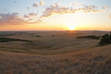 Obraz premium The horizon glows brilliantly at sunrise, casting golden light over the endless plains and fields, as scattered clouds drift across the gently waking sky.