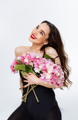 Woman with pink flowers in bright studio. A joyful woman in a black outfit embraces vibrant pink flowers, showcasing her radiant smile and lively spirit.