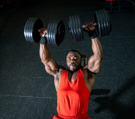 Man does overhead dumbbell press at gym. A muscular man lifts heavy dumbbells overhead in a gym,...