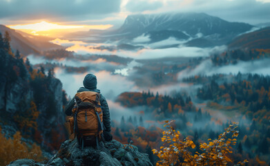Fototapeta premium Hiker gazing at sunrise over misty mountain valley. A lone hiker watches the sunrise illuminating a mist-covered valley, surrounded by autumn foliage and rocky terrain.