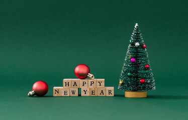 Christmas composition with Christmas tree, red Xmas baubles and wooden blocks with text Happy New Year on green background. Minimal Christmas and New Year concept. Creative festive holiday layout.