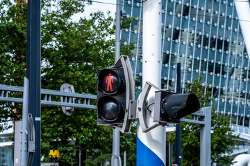 A vibrant red pedestrian signal on a city traffic light positioned against a backdrop of modern architecture and greenery, indicating 'stop' for street crossing in Rotterdam