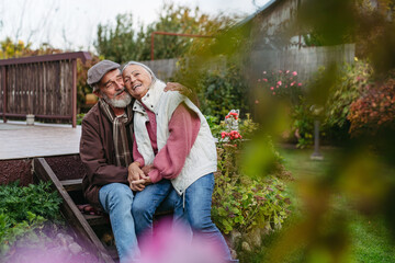 Fototapeta premium Portrait of beautiful senior couple outdoors in an autumn garden. Elderly husband and wife are embracing each other.