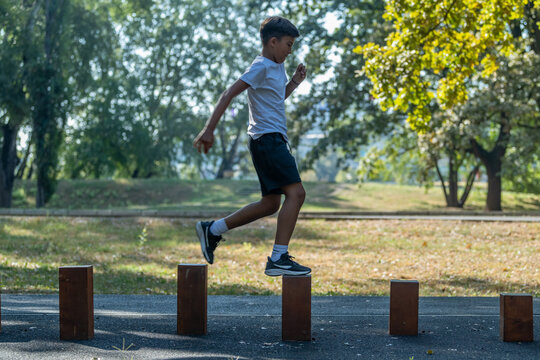 Young boy participates in outdoor physical activity, balancing on wooden stumps. Engaging in this fun exercise, he builds coordination and strength
