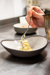 A close-up of a hand holding a spoon, serving cooked grains into a bowl on a kitchen counter. The image captures the motion and texture of the grains, emphasizing a home-cooked meal preparation.