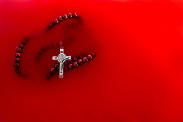 Red wooden rosary. Catholic rosary floating in red water, a symbol of sacrifice, suffering.