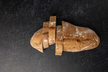 Artisan sliced bread in rustic style, arranged neatly on a dark, textured surface that adds a contrast highlighting the bread's crust and crumb textures vividly.