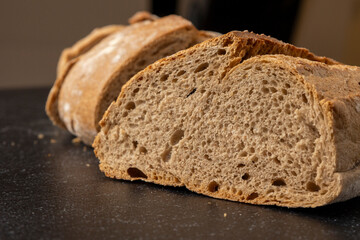 Artisan sliced bread in rustic style, arranged neatly on a dark, textured surface that adds a contrast highlighting the bread's crust and crumb textures vividly.