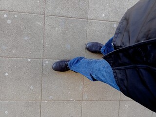 Down look of a male and his shoes on the asphalt ground.