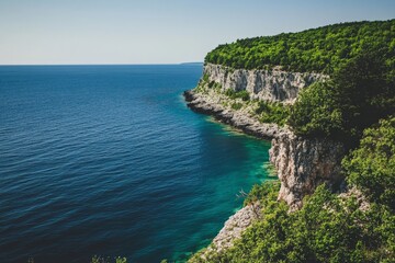 A picturesque view of a lush green cliffside sloping into a calm blue sea, showcasing nature’s vibrant colors under a clear sky, epitomizing tranquility and relaxation.