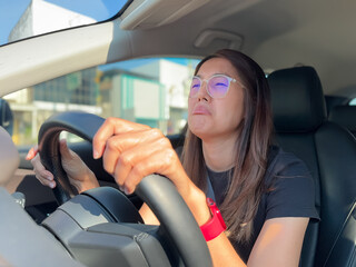 Front view of asian Thai woman driving a car with funny boring and unhappy  face, hand holding...