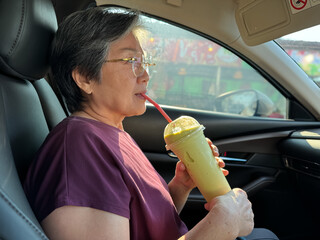 Happy old asian woman holding avocado frappe juice, showing thumbs up, while sitting and traveling...