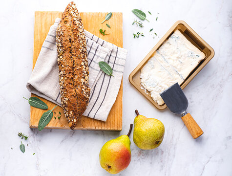  Italian Gorgonzola cheese (dolce) for recipes with pears, aromatic herbs served with healthy integral grain bread on a white marble background. Italian cheeses, traditions of Northern Italy, winter b